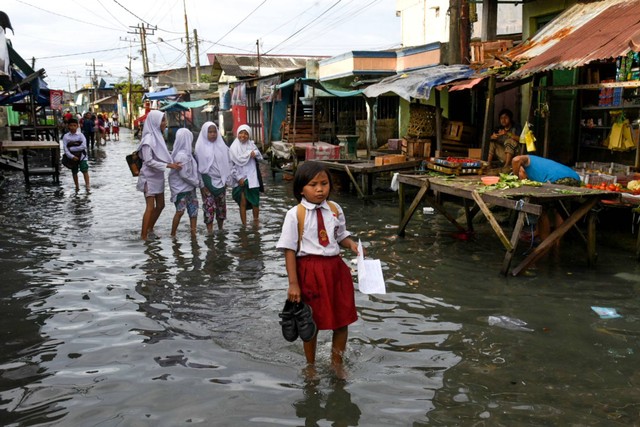 Sejumlah pelajar melintasi genangan air akibat banjir rob di Bagan Deli, Belawan, Kota Medan, Sumatera Utara, Selasa (25/10/2022). Foto: Fransisco Carolio/ANTARA FOTO