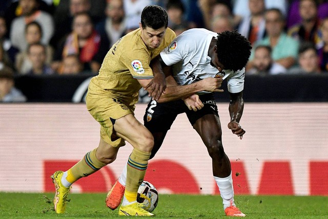 Pemain Valencia Thierry Correia beraksi bersama pemain FC Barcelona Robert Lewandowski di Stadion Mestalla, Valencia, Spanyol, Sabtu (29/10/2022). Foto: Pablo Morano/REUTERS