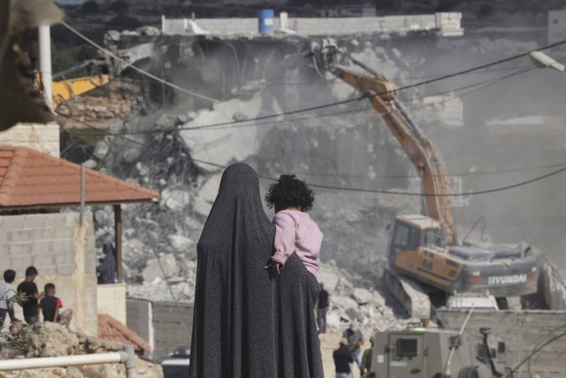 Seorang wanita Palestina menggendong bayi perempuan saat melihat buldoser tentara Israel menghancurkan sebuah bangunan di Hebron, Palestina, Senin (31/10/2022). Foto: Hazem Bader/AFP