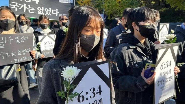Para pengunjuk rasa di dekat lokasi kejadian di Itaewon memegang posters bertuliskan: "Pada 6:34 negara tidak hadir [untuk para korban]"