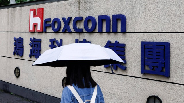 Seorang wanita membawa payung berjalan melewati logo Foxconn di luar gedung perusahaan di Taipei, Taiwan Senin (31/10/2022). Foto: Carlos Garcia Rawlins