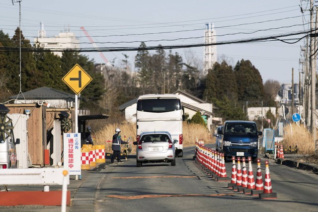 Seorang penjaga keamanan bertugas memeriksa izin khusus bagi pengendara di pos perlintasan untuk memasuki kota Okuma, prefektur Fukushima. Sebagian bangunan di PLTN Fukushima Daiichi terlihat pada latar belakang. (Dok: Hiro Komae)