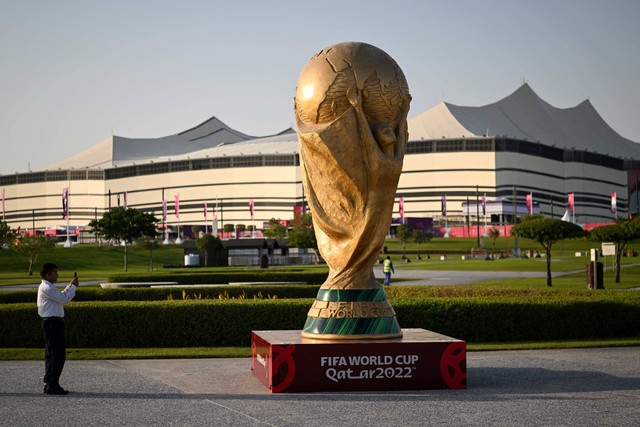 Seorang pria mengambil gambar replika trofi Piala Dunia FIFA di depan Stadion Al-Bayt di al-Khor jelang turnamen sepak bola Piala Dunia FIFA Qatar 2022 pada Kamis (10/11/2022). Foto: Kirill Kudryavtsev/AFP