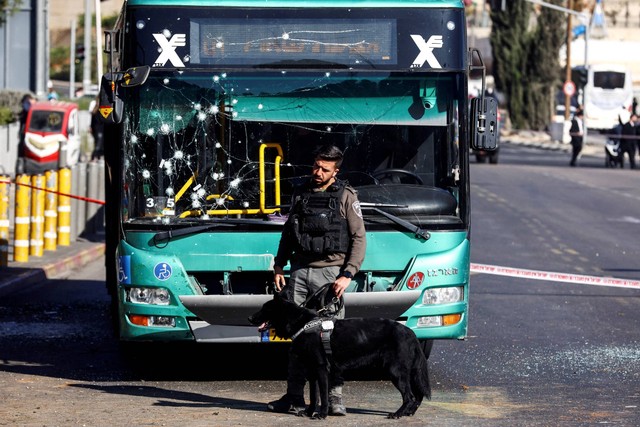 Seorang petugas polisi memegang seekor anjing di dekat bus yang rusak setelah ledakan di halte bus di Yerusalem, Rabu (23/11/2022). Foto: Ronen Zvulun/REUTERS