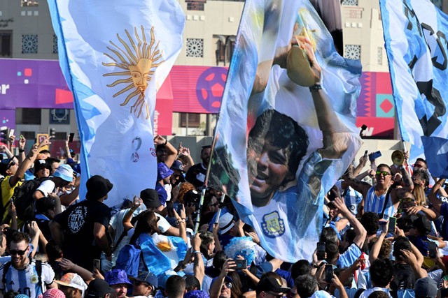 Penggemar Argentina memegang bendera legenda sepak bola Diego Maradona saat mereka berkumpul di acara "Banderazo" mendukung tim mereka, di promenade Corniche Doha di Doha, pada 21 November 2022. Foto: Pablo Porciuncula/AFP