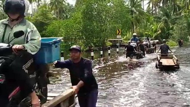 Warga di Kabupaten Bengkalis, Riau, membantu pengguna jalan melintasi jalanan yang digenangi banjir