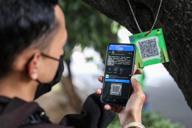 Warga melihat data pohon dengan memindai QR code yang terpasang pada pohon tersebut di Jalan Ir H Juanda, Depok, Jawa Barat, Sabtu (26/11/2022). Foto: Asprilla Dwi Adha/Antara Foto