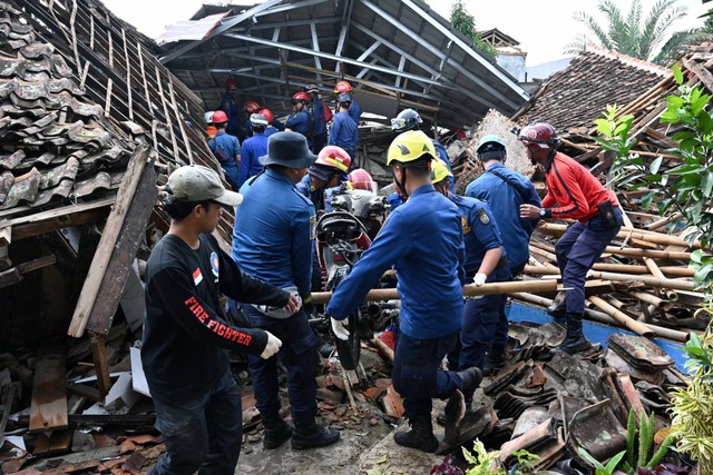 Petugas penyelamat mengeluarkan sepeda motor saat mereka bekerja untuk menemukan anak hilang yang diyakini terjebak di reruntuhan rumah yang runtuh di Cugenang di Cianjur, Jawa Barat, Kamis (24/11/2022). Foto: Adek Berry/AFP