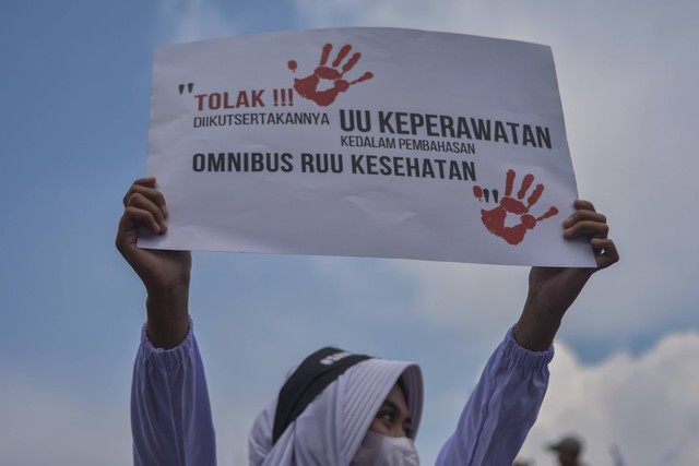 Seorang tenaga kesehatan membentangkan poster saat berunjuk rasa menolak RUU Omnibus law Kesehatan di depan Gedung Parlemen, Senayan, Jakarta, Senin (28/11/2022). Foto: Sulthony Hasanuddin/Antara Foto