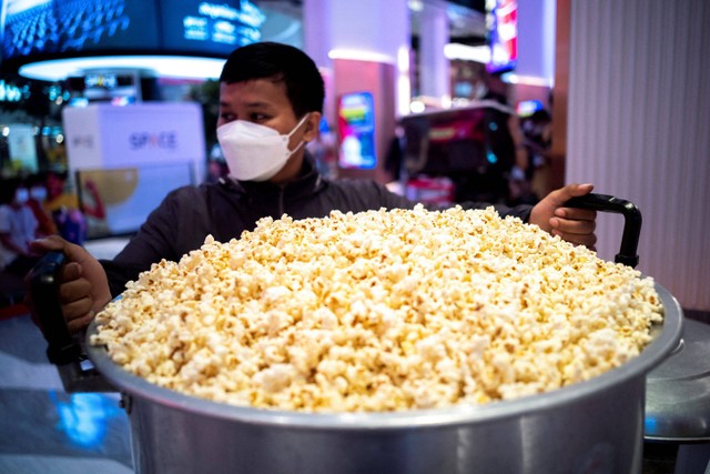 Seorang pria membawa panci berisi popcorn di depan bioskop department store di Bangkok, Thailand. Foto: Athit Perawongmetha/REUTERS