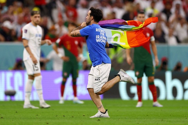 Seorang suporter yang mengenakan kaos bertuliskan 'Respect for Iranian Women' dan memegang bendera pelangi berlari ke lapangan saat pertandingan Timnas Portugal melawan Timnas Uruguay di Stadion Lusail, Lusail, Qatar. Foto: Kai Pfaffenbach/REUTERS