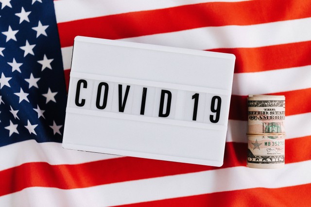 Photo by :  Karolina Grabowska https://www.pexels.com/photo/signboard-with-covid-19-title-on-american-flag-with-banknotes-4386340/
