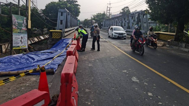 Anggota Sat Lantas Polres Bojonegoro saat memasang garis polisi dan rambu pengaman pembatas jalan, di Jembatan Jetak, Kota Bojonegoro, yang alami longsor. Minggu (04/12/2022) (Foto: Dok Istimewa)