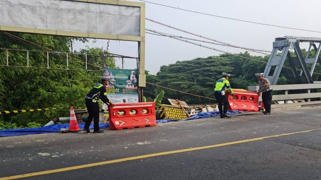 Anggota Sat Lantas Polres Bojonegoro saat memasang garis polisi dan rambu pengaman pembatas jalan, di Jembatan Jetak, Kota Bojonegoro, yang alami longsor. Minggu (04/12/2022) (Foto: Dok Istimewa)