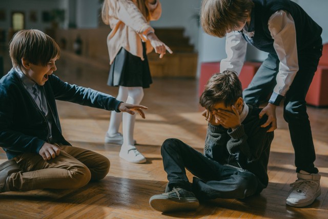 Foto oleh Mikhail Nilov: https://www.pexels.com/photo/children-finger-pointing-at-a-boy-sitting-on-a-wooden-floor-7929446/