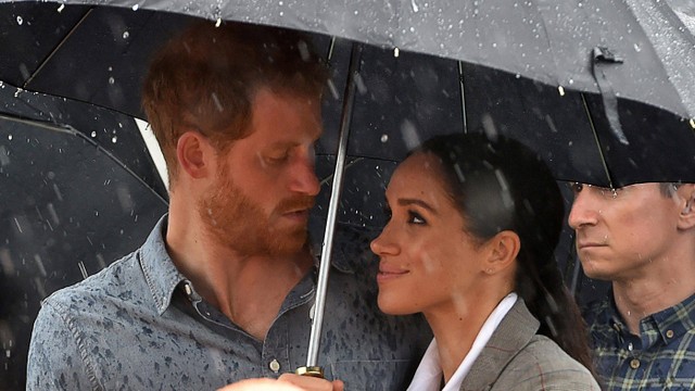 Pangeran Harry dari Inggris berbicara kepada masyarakat didampingi istrinya Meghan, Duchess of Sussex memegang payung di bawah hujan lebat di pedalaman Dubbo di Australia pada 17 Oktober 2018. Foto: Peter Parks/Pool / AFP