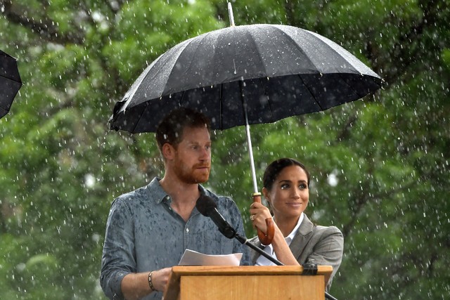 Pangeran Harry dari Inggris berbicara kepada masyarakat didampingi istrinya Meghan, Duchess of Sussex memegang payung di bawah hujan lebat di pedalaman Dubbo di Australia pada 17 Oktober 2018. Foto: Peter Parks/Pool / AFP