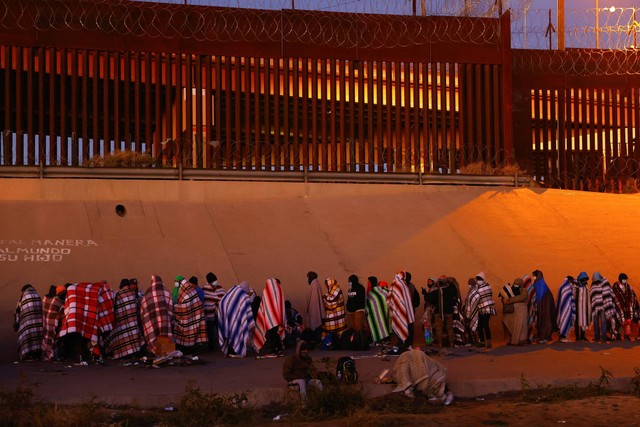 Migran mengantri di dekat tembok perbatasan setelah menyeberangi sungai Rio Bravodi kota El Paso, Texas, AS, seperti yang terlihat dari Ciudad Juarez, Meksiko, Selasa (13/12/2022). Foto: Jose Luis/Reuters