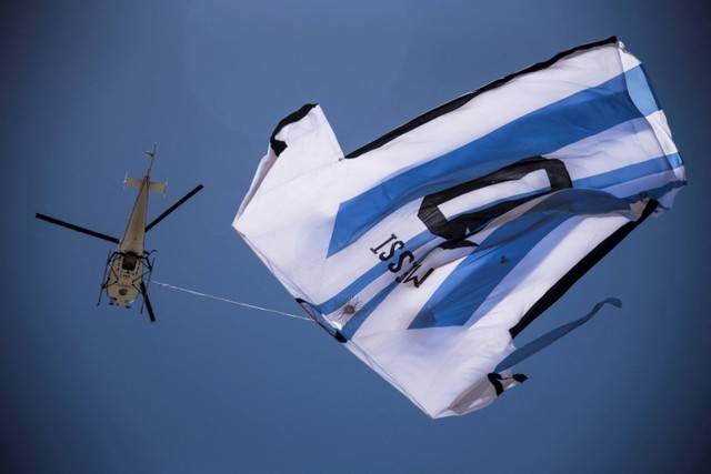 Sebuah helikopter membawa t-shirt raksasa penyerang Argentina Lionel Messi di atas Rosario, Argentina, pada Selasa (13/12/2022). Foto: STR/AFP