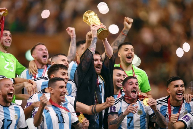 Pemain Argentina Lionel Messi berselebrasi dengan trofi bersama rekan setimnya setelah memenangkan Piala Dunia 2022, di Stadion Lusail, Lusail, Qatar, Minggu (18/12/2022). Foto: Hannah McKay/REUTERS