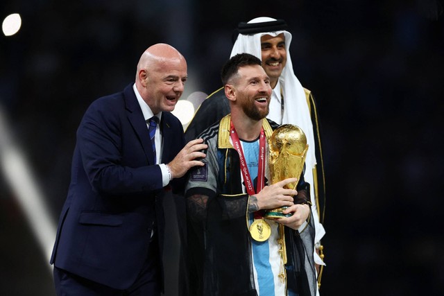 Pemain Argentina Lionel Messi diberikan trofi oleh presiden FIFA Gianni Infantino dan Emir Qatar Sheikh Tamim bin Hamad Al Thani setelah Argentina memenangkan Piala Dunia 2022, di Stadion Lusail, Lusail, Qatar, Minggu (18/12/2022). Foto: Carl Recine/REUTERS