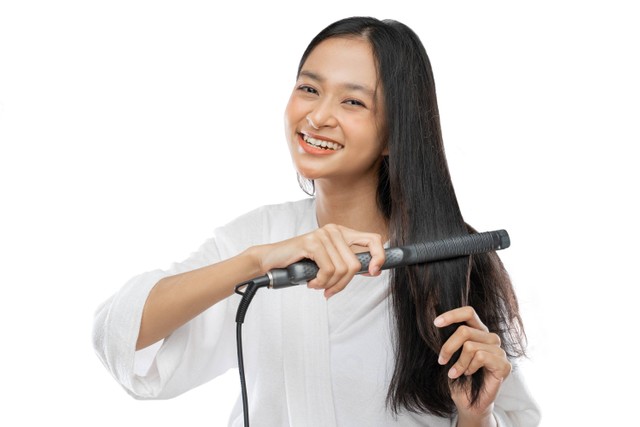Ilustrasi perempuan meluruskan rambut keriting dengan catokan. Foto: Shutterstock