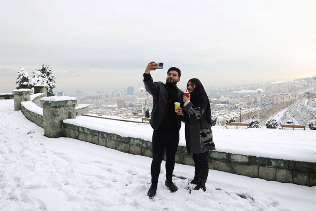 Pasangan Iran berswafoto saat hujan salju pertama di sebuah taman di Teheran, Iran, Sabtu (24/12/2022). Foto: Majid Asgaripour/WANA/Reuters