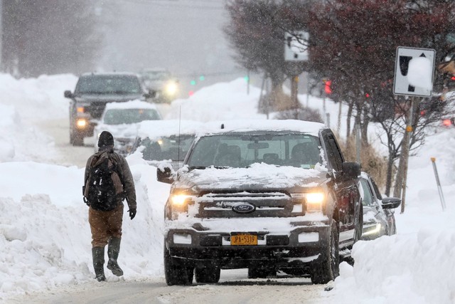Seorang pria berjalan di jalan tertutup salju saat mobil melintas, usai badai musim dingin melanda wilayah Buffalo, di Amherst, New York, AS, Senin (26/12/2022). Foto: Brendan McDermid/REUTERS