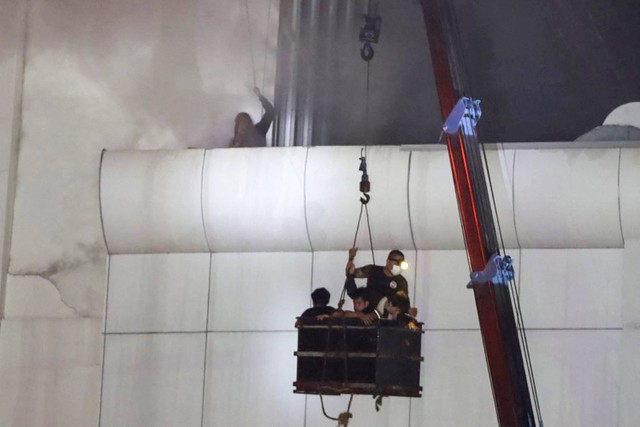 Petugas penyelamat menurunkan orang ke tanah saat api berkobar di kasino hotel Grand Diamond City di Poipet, Kamboja, Thailand, Kamis (29/12/2022). Foto: STR/AFP