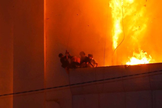 Orang-orang berkumpul di langkan saat api membakar di sekitar mereka di hotel-kasino Grand Diamond City di Poipet, Kamboja, Thailand, Kamis (29/12/2022). Foto: STR/AFP