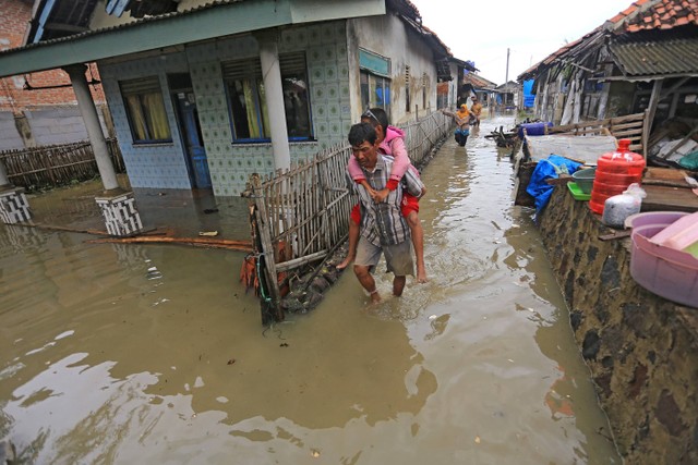 Warga melintasi genangan banjir rob di desa Kertawangunan, Kandanghaur, Indramayu, Jawa Barat, Sabtu (31/12/2022). Foto: Dedhez Anggara/Antara Foto