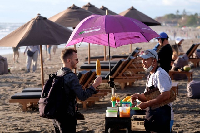 Wisatawan mancanegara membeli jagung bakar saat mengunjungi objek wisata Pantai Berawa, Kuta Utara, Badung, Bali, Selasa (10/1/2023). Foto: Nyoman Hendra Wibowo/Antara Foto