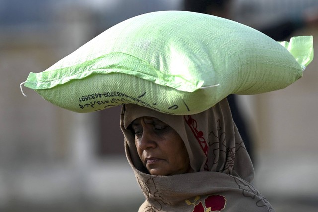 Seorang wanita membawa sekarung tepung terigu setelah membeli dengan harga yang diatur pemerintah di Islamabad, Pakistan, Selasa (10/1/2023). Foto: Aamir Qureshi/AFP