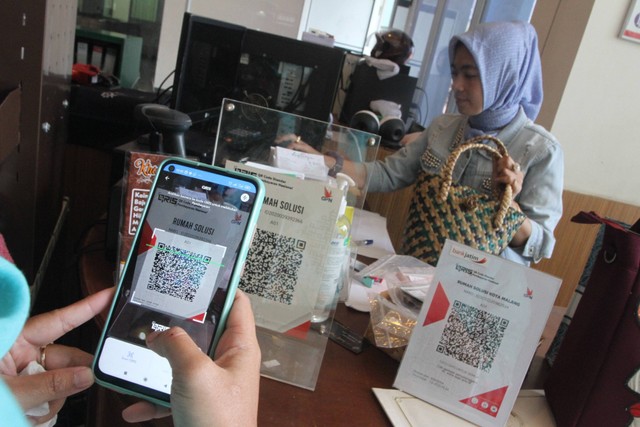 Seorang konsumen menggunakan layanan pembayaran digital Quick Response Code Indonesia Standard (QRIS) saat membeli produk di gerai Rumah Solusi UMKM, Malang, Jawa Timur, Kamis (12/1/2023). Foto: Ari Bowo Sucipto/Antara Foto