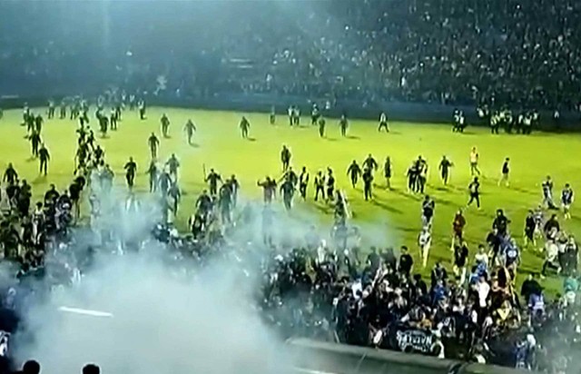 Tangkapan layar video AFPTV yang diambil pada 1 Oktober 2022 ini menunjukkan gas air mata di tengah orang-orang berlarian di lapangan usai pertandingan sepak bola antara Arema FC dan Persebaya Surabaya di Stadion Kanjuruhan, Malang, Jawa Timur. Foto: AFPTV
