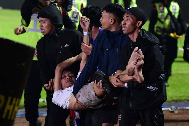 Sekelompok orang menggendong seorang pria usai pertandingan sepak bola antara Arema FC dan Persebaya Surabaya di stadion Kanjuruhan, Malang, Jawa Timur (1/10/2022) Foto: STR/AFP