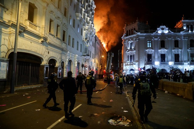 Petugas polisi berjalan menuju gedung yang terbakar selama protes 'Ambil alih Lima', di Lima, Peru, Kamis (19/1/2023). Foto: Sebastian Castaneda/REUTERS