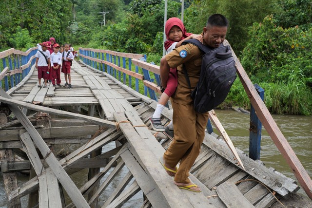 Seorang guru menggendong siswa SD Negeri 1 Alaaha saat menyeberangi jembatan rusak di Desa Alaaha, Kecamatan Ueesai, Kolaka Timur, Sulawesi Tenggara, Sabtu (21/1/2023). Foto: Jojon/Antara Foto