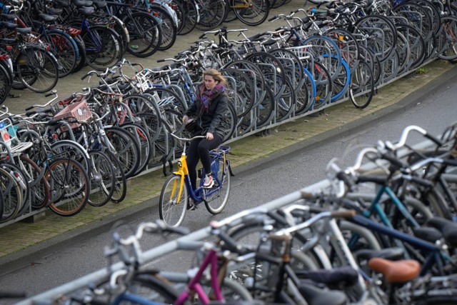 Seorang wanita mengendarai sepeda di luar tempat parkir di Amsterdam, Belanda barat, pada 25 November 2021. Foto: SEBASTIEN BOZON / AFP