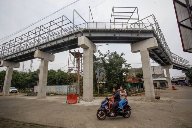 Warga melintas di depan proyek pembangunan jembatan multiguna (skybridge) di Bojonggede, Kabupaten Bogor, Jawa Barat, Senin (30/1/2023). Foto: Yulius Satria Wijaya/Antara Foto