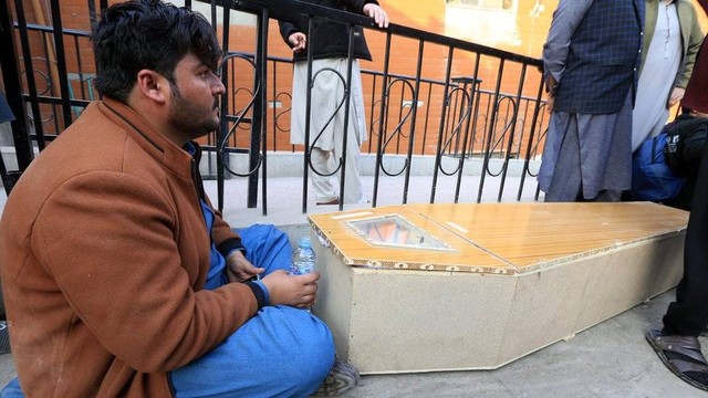 Seorang pria duduk di sebelah sebuah peti jenazah korban ledakan masjid di Peshawar, Pakistan.