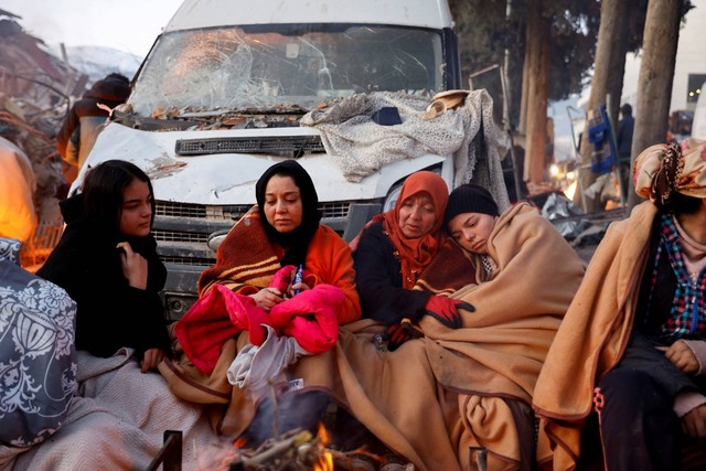 Orang-orang duduk di sekitar api di samping puing-puing dan kerusakan di dekat lokasi bangunan yang runtuh setelah gempa bumi, di Kahramanmaras, Turki, Rabu (8/2/2023). Foto: Suhaib Salem/REUTERS