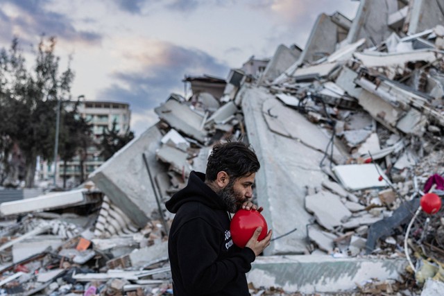 Ogun Sever Okur, meniup balon yang akan digantung di atas puing-puing bangunan yang runtuh di Antakya, Hatay, Turki.  Foto: Sameer Al-DOUMY / AFP