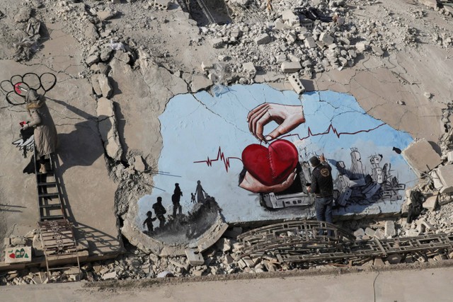Seniman Suriah Aziz Asmar dan Salam Hamed melukis seni jalanan di atas puing-puing bangunan yang rusak akibat gempa di kota Jandaris, Suriah.  Foto: Khalil Ashawi/REUTERS