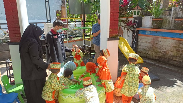 mendampingi anak-anak bermain di kolam air untuk bermain perahu layar yang mereka buat