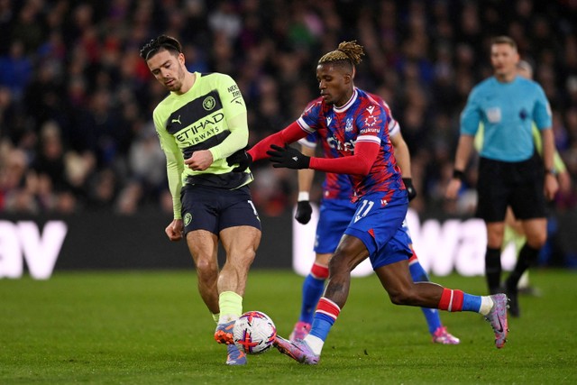 Pemain Manchester City Jack Grealish berebut bola dengan pemain Crystal Palace Wilfried Zaha pada pertandingan lanjutan Liga Inggris di Selhurst Park, London, Inggris, Minggu (12/3/2023).  Foto: Tony Obrien/REUTERS