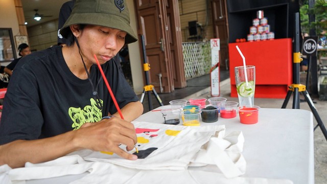 Aksi seniman lokal asal Kota Prabumulih yang sedang melukis merchandise dalam selesi parade band, Minggu (12/3) Foto: abp/Urban Id