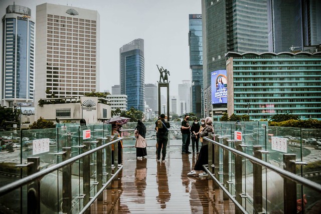 Sejumlah warga berada di anjungan halte Bundaran Hotel Indonesia saat hujan ringan, Jakarta. Foto: Jamal Ramadhan/kumparan
