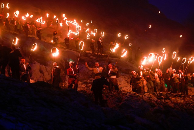 Warga suku Kurdi Irak membawa obor api, saat mereka merayakan Hari Nowruz, sebuah festival yang menandai hari pertama musim semi dan Tahun Baru Persia, di kota Akra dekat Duhok, di Kurdistan, Irak 20 Maret 2023. Foto: Alaa Al-Marjani/Reuters