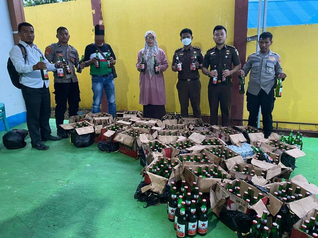 MSJ alias ayah (kaos bermotif hijau putih hitam) saat berpose bersama barang bukti minuman keras jenis bir miliknya, didampingi petugas di Pengadilan Negeri Soasio, Kota Tidore Kepulauan, Maluku Utara. Foto: Istimewa